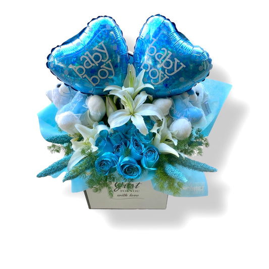 A floral gift basket for a baby boy, featuring a bouquet of blue flowers, white lilies, and two blue teddy bears with the text 'Baby Boy' on them.