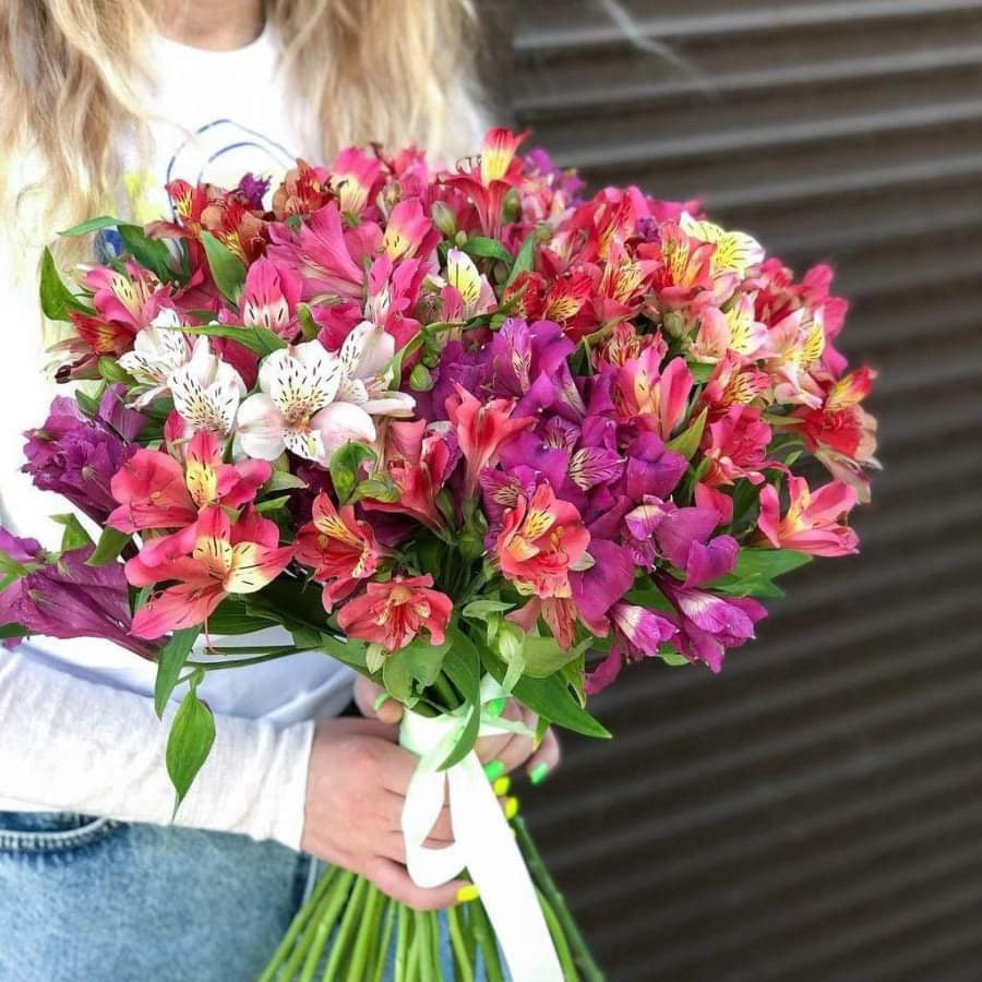 A bouquet from the premium flowershop flowershopping.gr in Athens that consists of various flowers with predominantly pink and red petals, some with speckles, and green stems bundled together