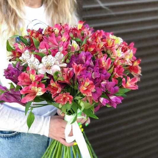 A bouquet from the premium flowershop flowershopping.gr in Athens that consists of various flowers with predominantly pink and red petals, some with speckles, and green stems bundled together